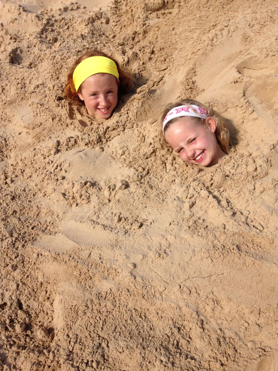Children in the sand on Wells beach, where you can hire our beach hut, "The Den"